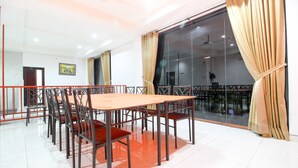 Un espace repas avec une longue table et des chaises, une grande fenêtre avec des rideaux et une vue sur le balcon extérieur.