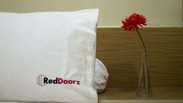 Een wit kussen met een RedDoorz logo en een heldere vaas met één rode bloem.