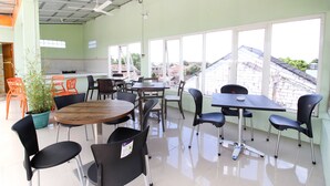 A spacious indoor dining area with multiple tables and chairs, large windows offering a view of the outside, and a ceiling fan. - RedDoorz Plus near Taman Sari (Yogyakarta)