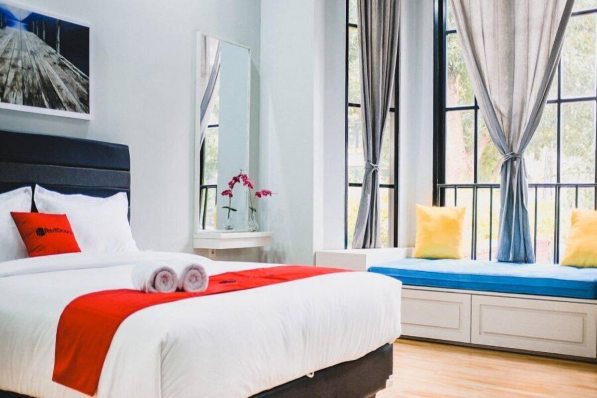 A hotel room with a bed, a window seat, a bedside table, and a mirror.