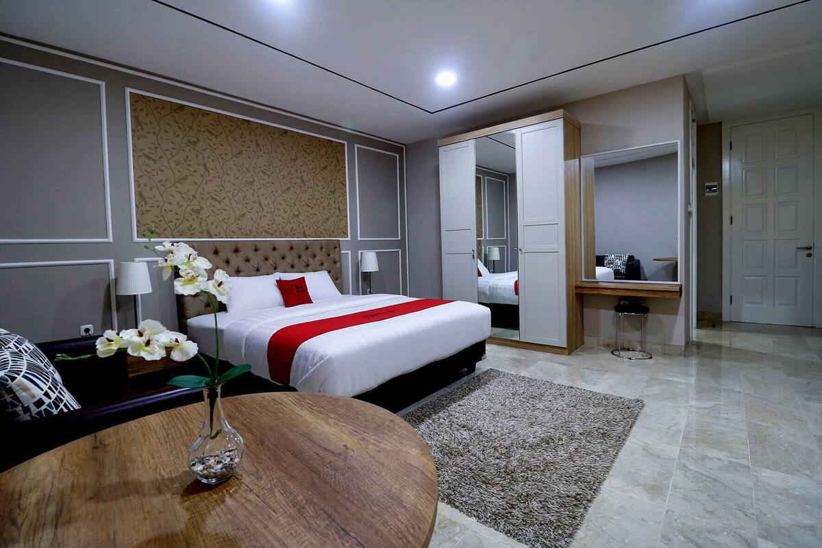 A hotel room with a bed, a desk, a chair, a round table, and a vase with flowers.