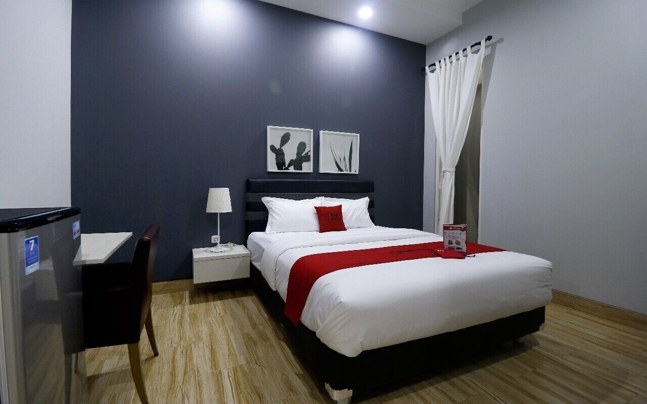 Una habitación de hotel con cama, escritorio, mesita de noche y lámpara de pared.