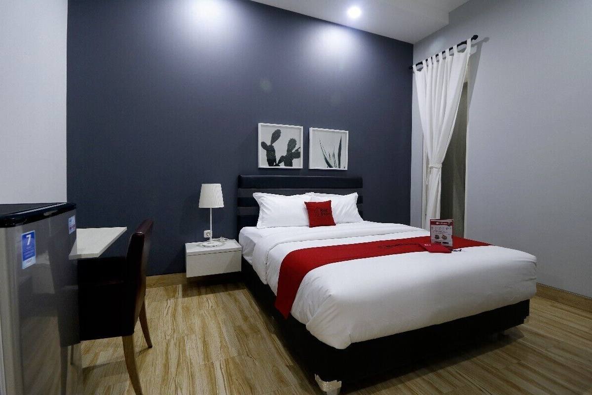 A hotel room with a bed, a desk, a nightstand, and a wall-mounted lamp.