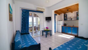 Una habitación con una cama, una mesa con flores, un televisor y una zona de cocina.