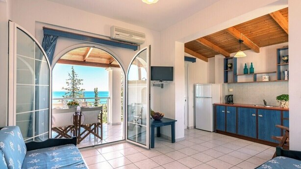 Una cocina moderna con techo de madera, un comedor con mesa y sillas, y vista al mar a través de un ventanal.