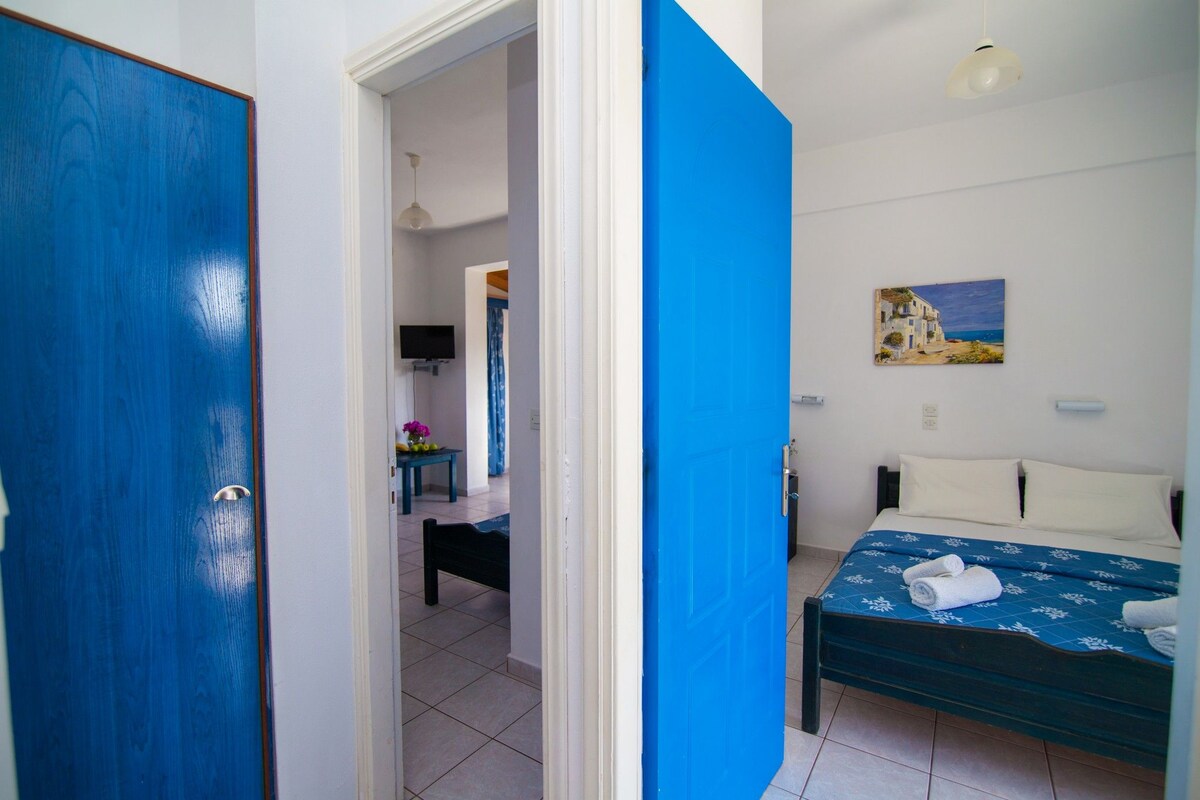 A bedroom with a bed, a painting on the wall, and a blue door.