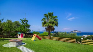 Un área verde bien cuidada con un parque infantil, una casita de juegos y una palmera.