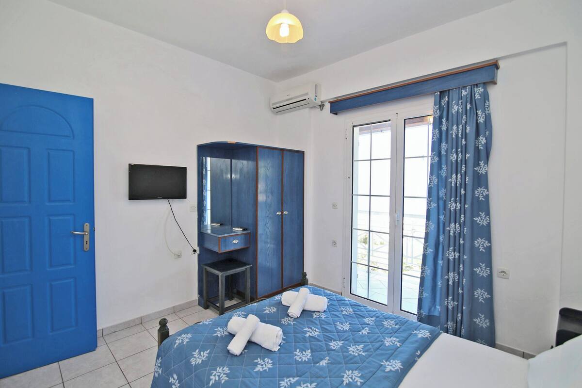 A bedroom with a blue door, a wardrobe, a bed with a blue floral bedspread, and a window with blue curtains.