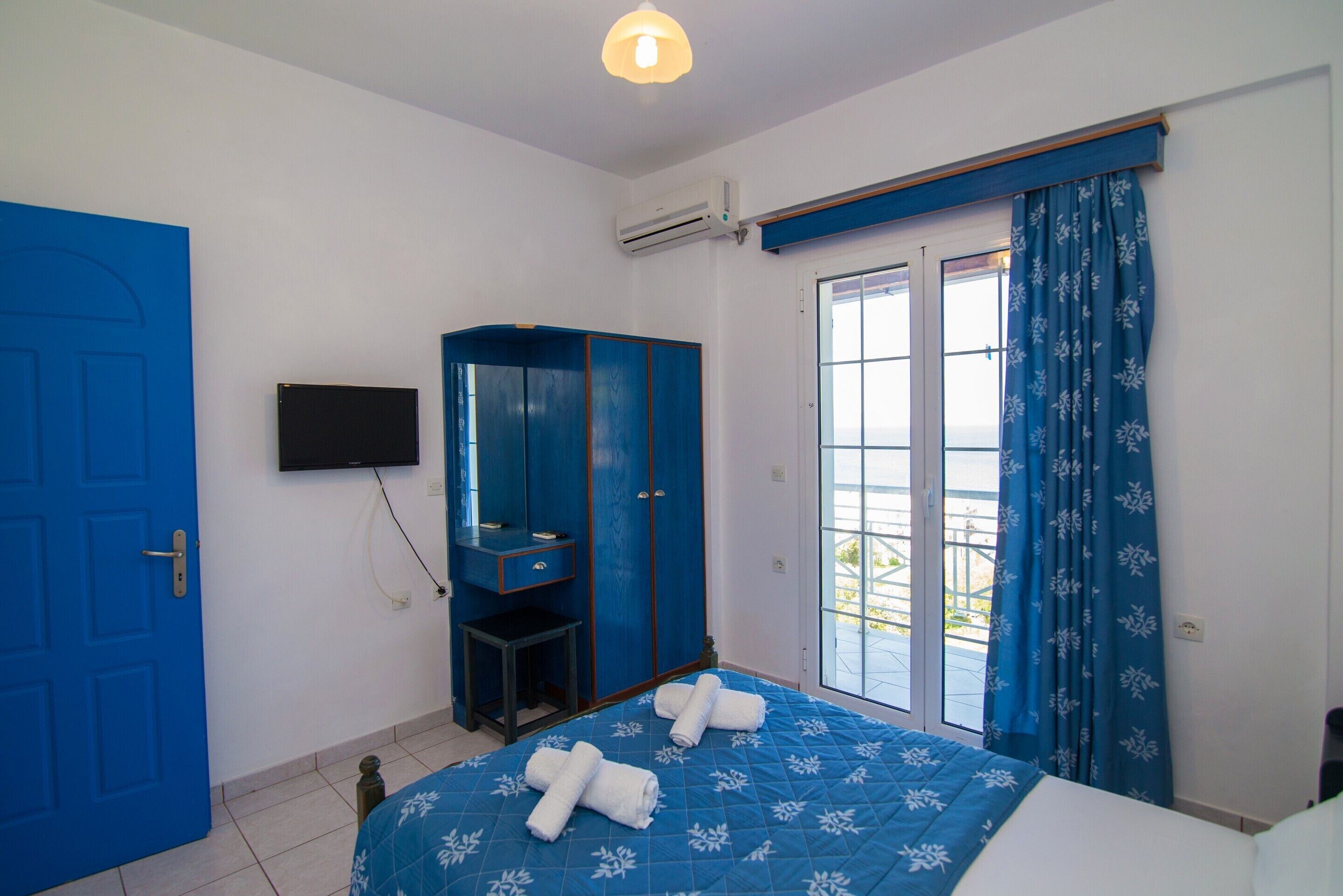 A bedroom with a bed, a wardrobe, a television, and a window with curtains.