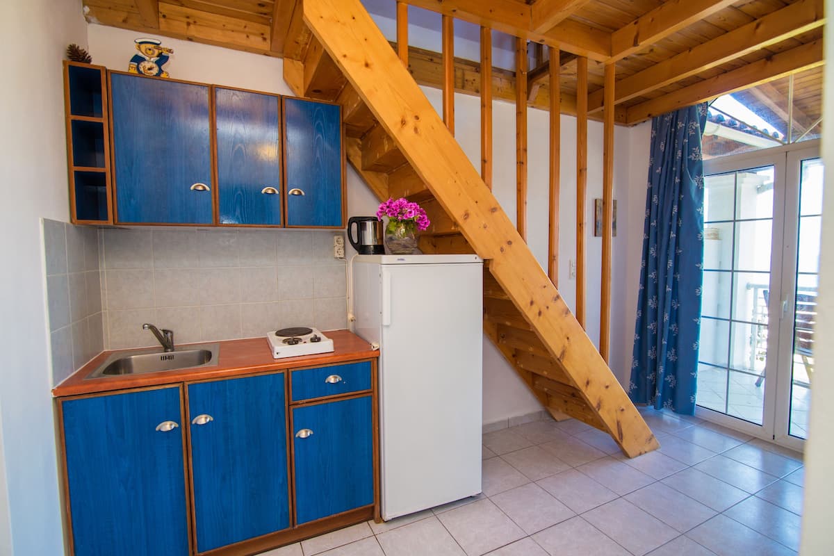 A compact kitchen with blue cabinets, a white refrigerator, and a wooden staircase.