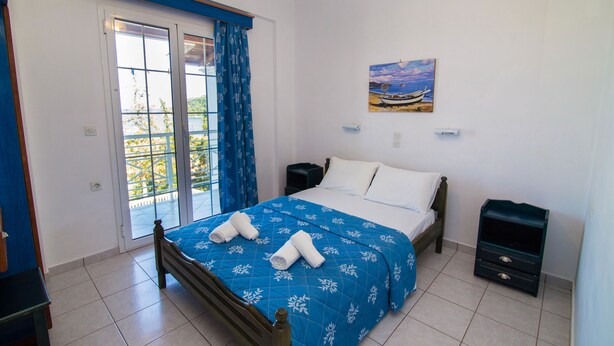 Une chambre à coucher comprenant un lit, une table de chevet, une commode, un tableau et une porte-fenêtre coulissante donnant sur un balcon.