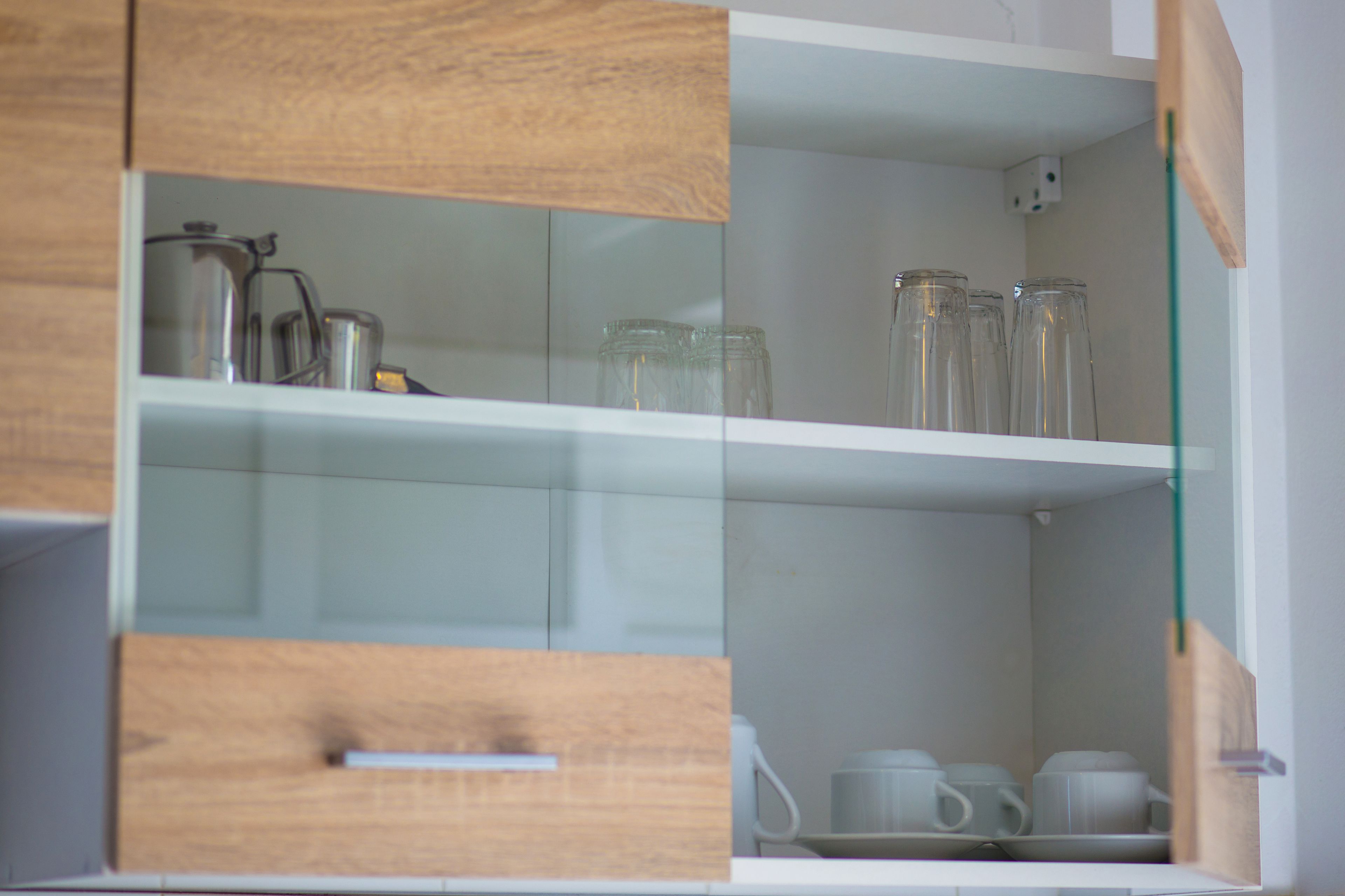Una cocina con armarios de madera, una repisa con puerta de vidrio y utensilios de cocina blancos.