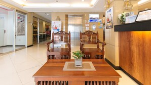 A reception area with a wooden reception desk, two wooden chairs, a small table with a plant, and a wall-mounted TV. - RedDoorz Plus @ Project 6 Quezon City (Quezon City)