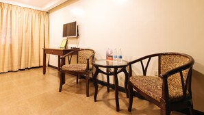 A small, furnished room with a wooden desk, two patterned chairs, a glass table, a television on the wall, and a curtain. - RedDoorz Plus @ Project 6 Quezon City (Quezon City)