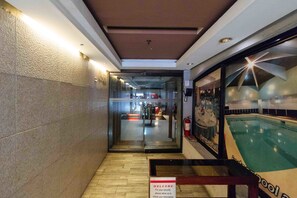 Um saguão de hotel com balcão de recepção, entrada por porta de vidro e área de piscina vis ível através do vidro.