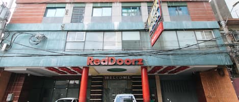 A building with a red and blue facade, a 'Welcome' sign, and several parked cars and motorcycles in front.