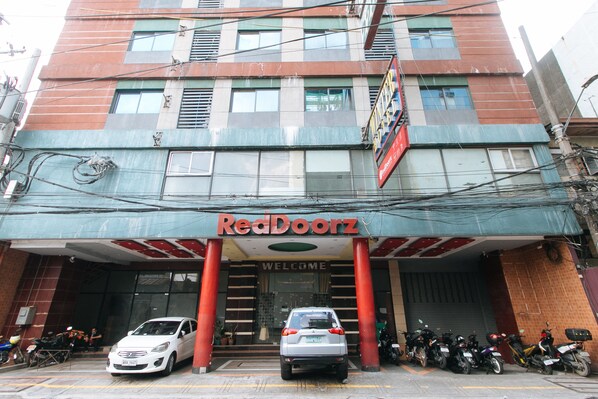 A building with a red and blue facade, a 'Welcome' sign, and several parked cars and motorcycles in front. - RedDoorz @ Winter Hotel Araneta (Quezon City)