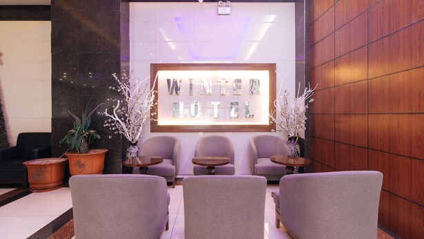 A lobby with a reception desk, three purple armchairs, two small round tables, and potted plants. - RedDoorz @ Winter Hotel Araneta (Quezon City)