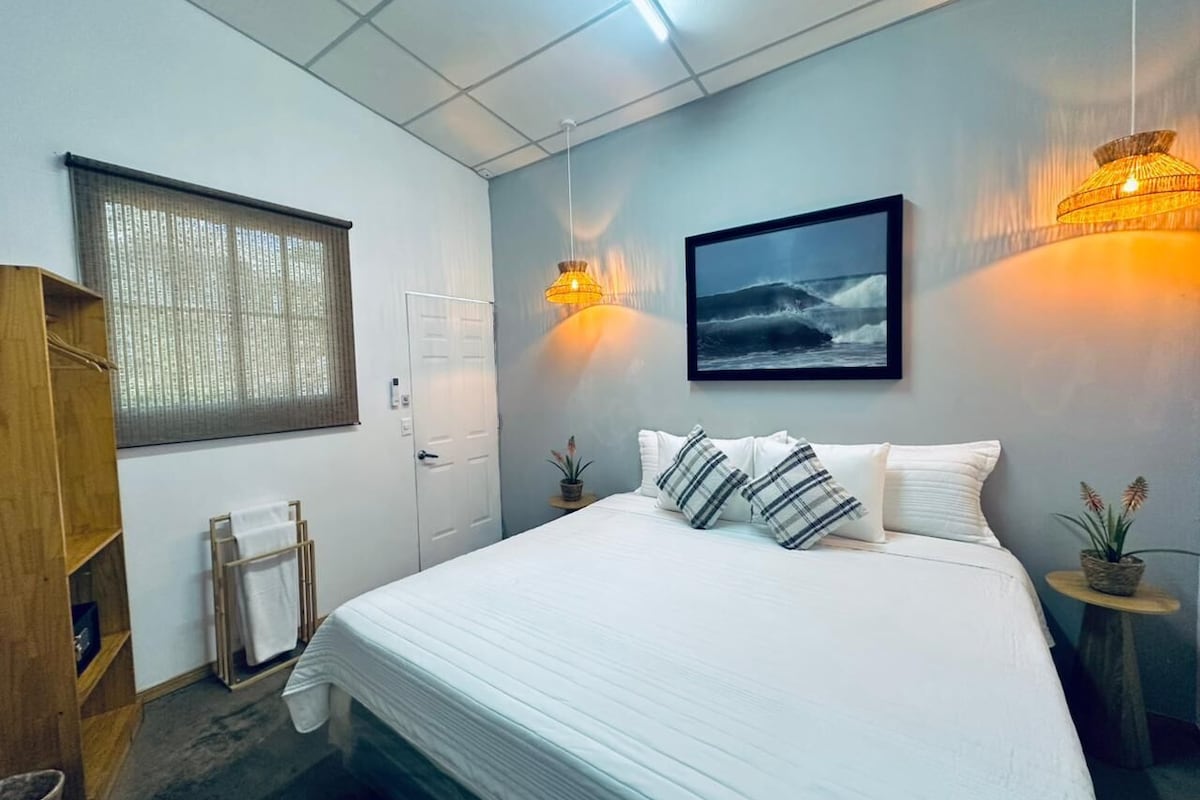 A bedroom with a bed, a window with blinds, a wall-mounted picture, and two bedside lamps.