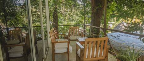 Un espacio de estar al aire libre techado, con mobiliario de madera y vistas a vegetación exuberante.
