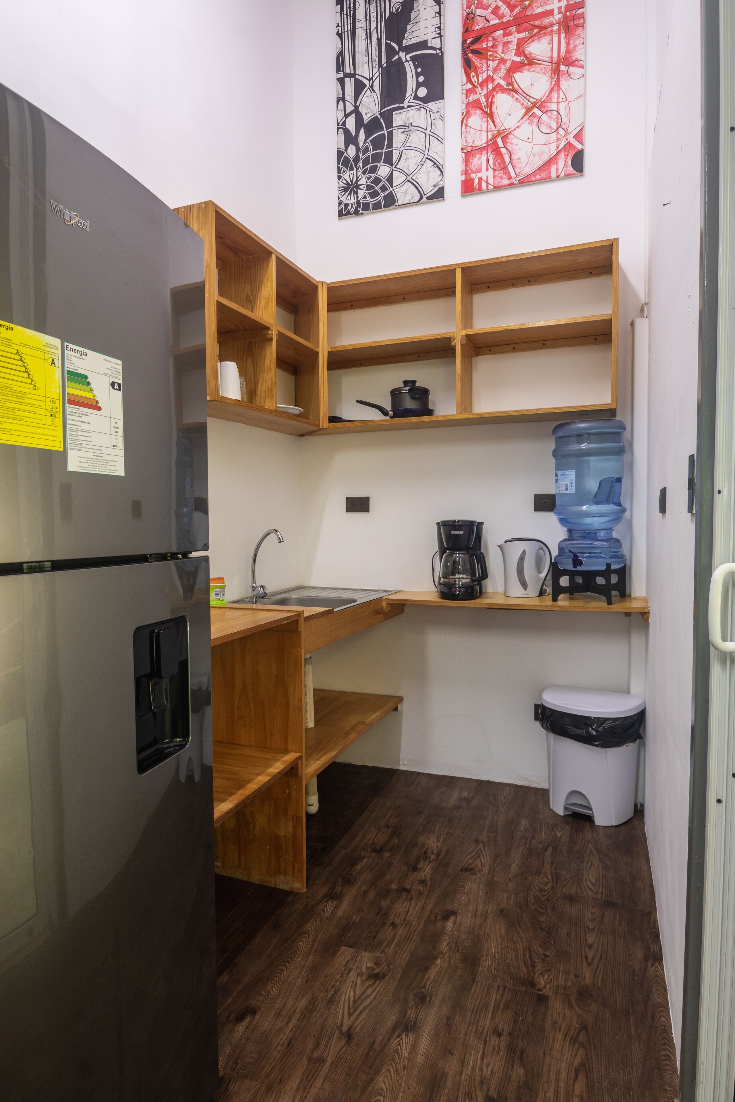 Eine kleine Küche mit einem Kühlschrank, Holzböden, einem Waschbecken und einem Wasserspender.