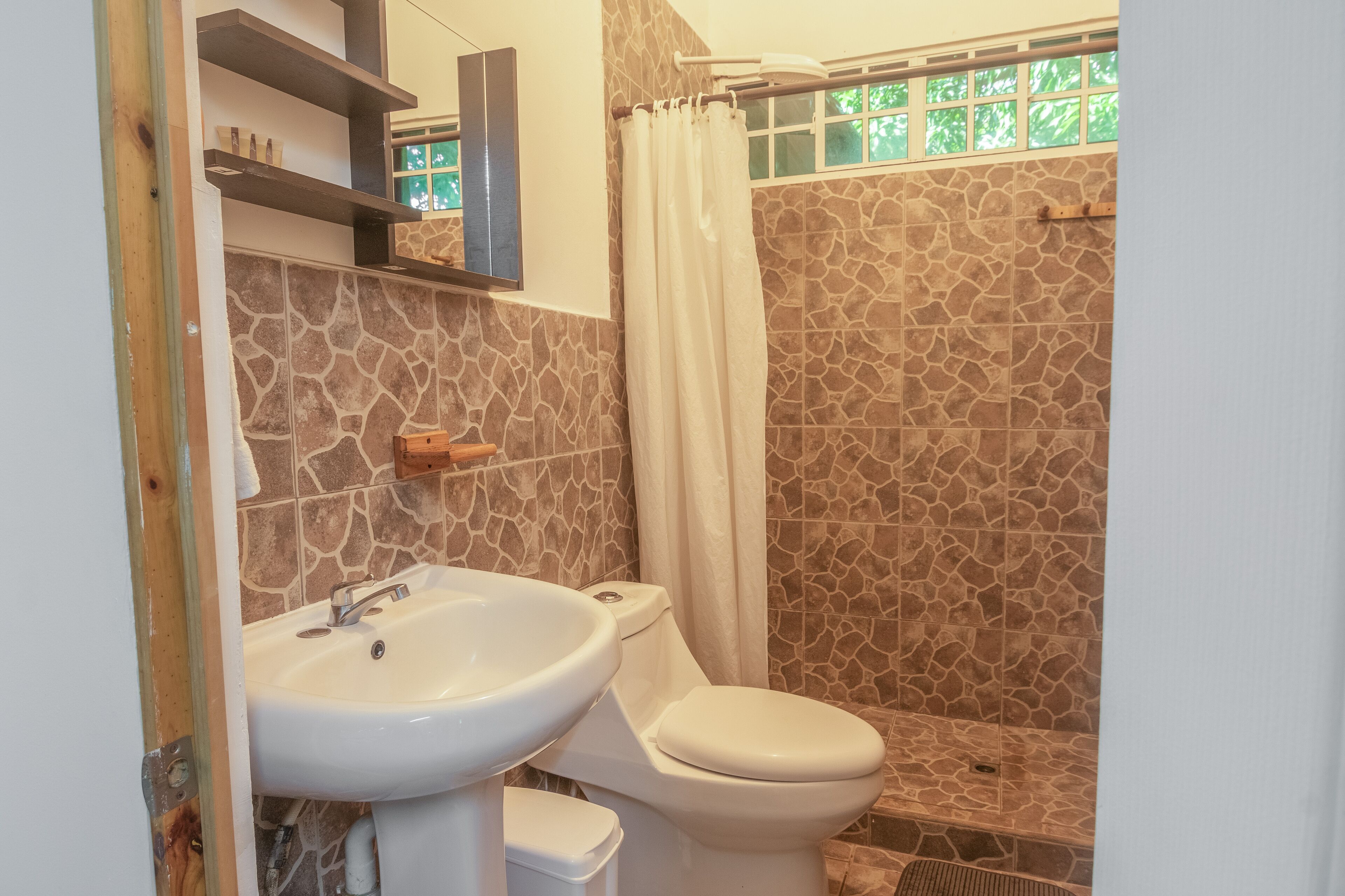 Un baño con ducha de baldosas de piedra, un lavabo blanco y un inodoro.
