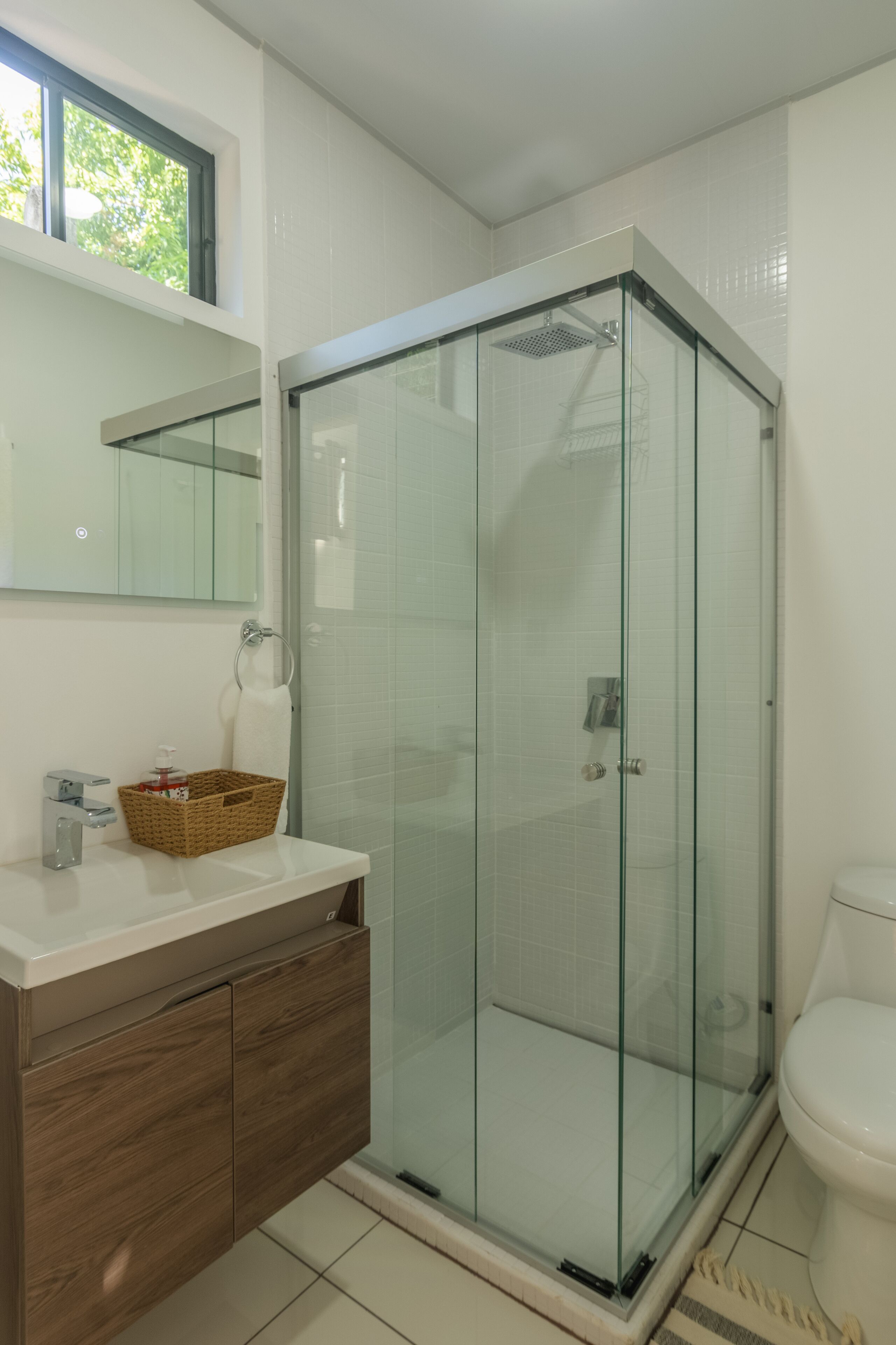 Ein modernes Badezimmer mit einer Duschkabine, einem weißen Waschbecken mit Holzschrank und einer Toilette.