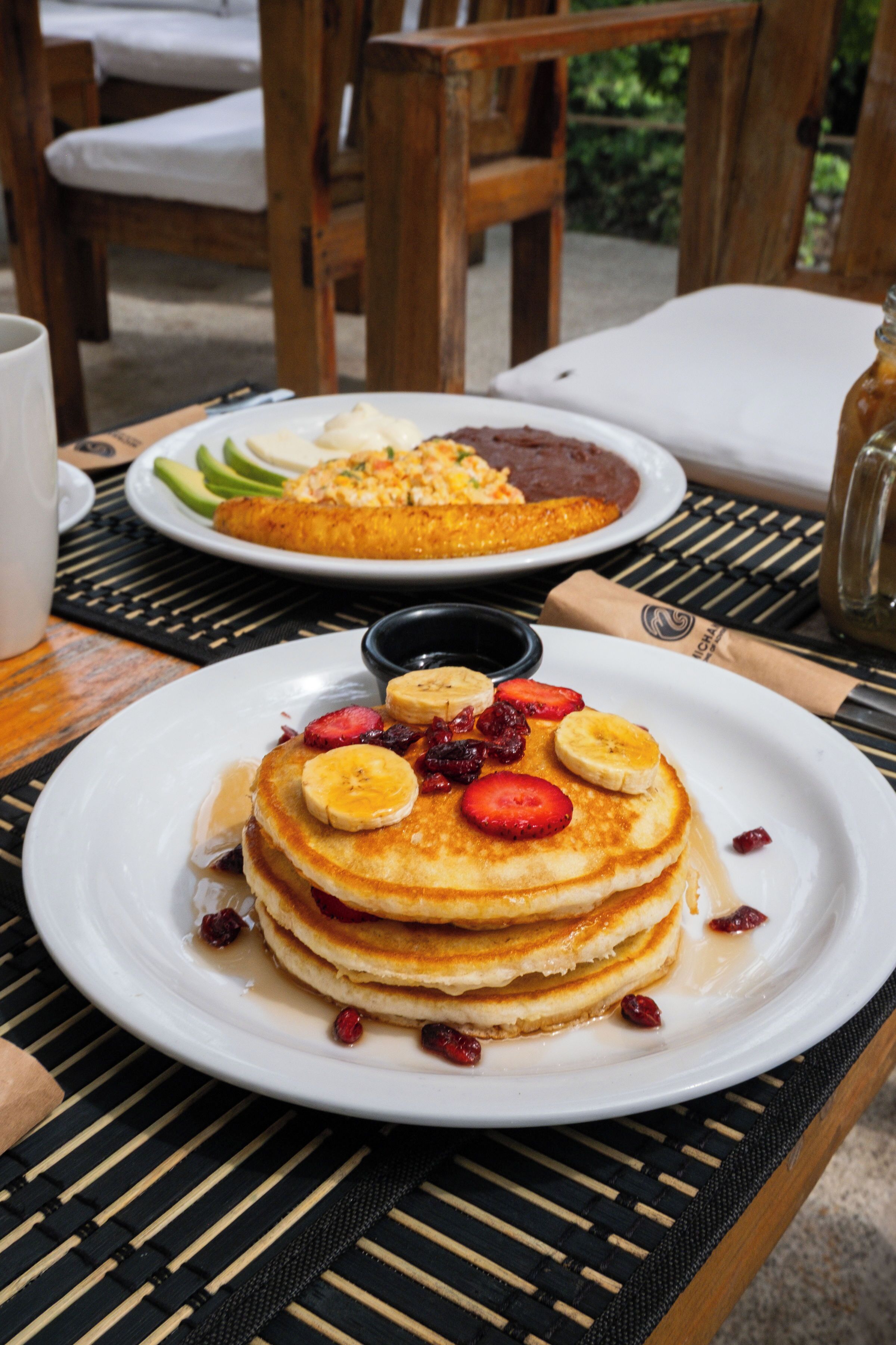A breakfast setting with pancakes, strawberries, and bananas on a white plate.