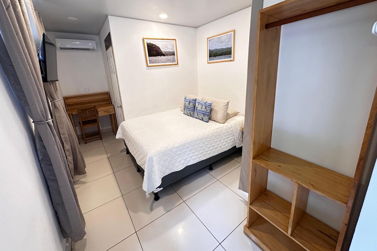 A bedroom with a bed, a wooden desk, a chair, and two framed pictures on the wall.