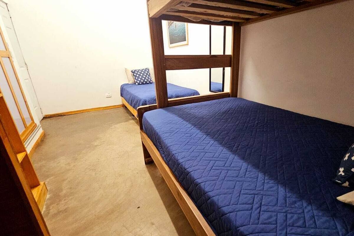 A room with two beds, one with a window, wooden beams, and a view of the outside.
