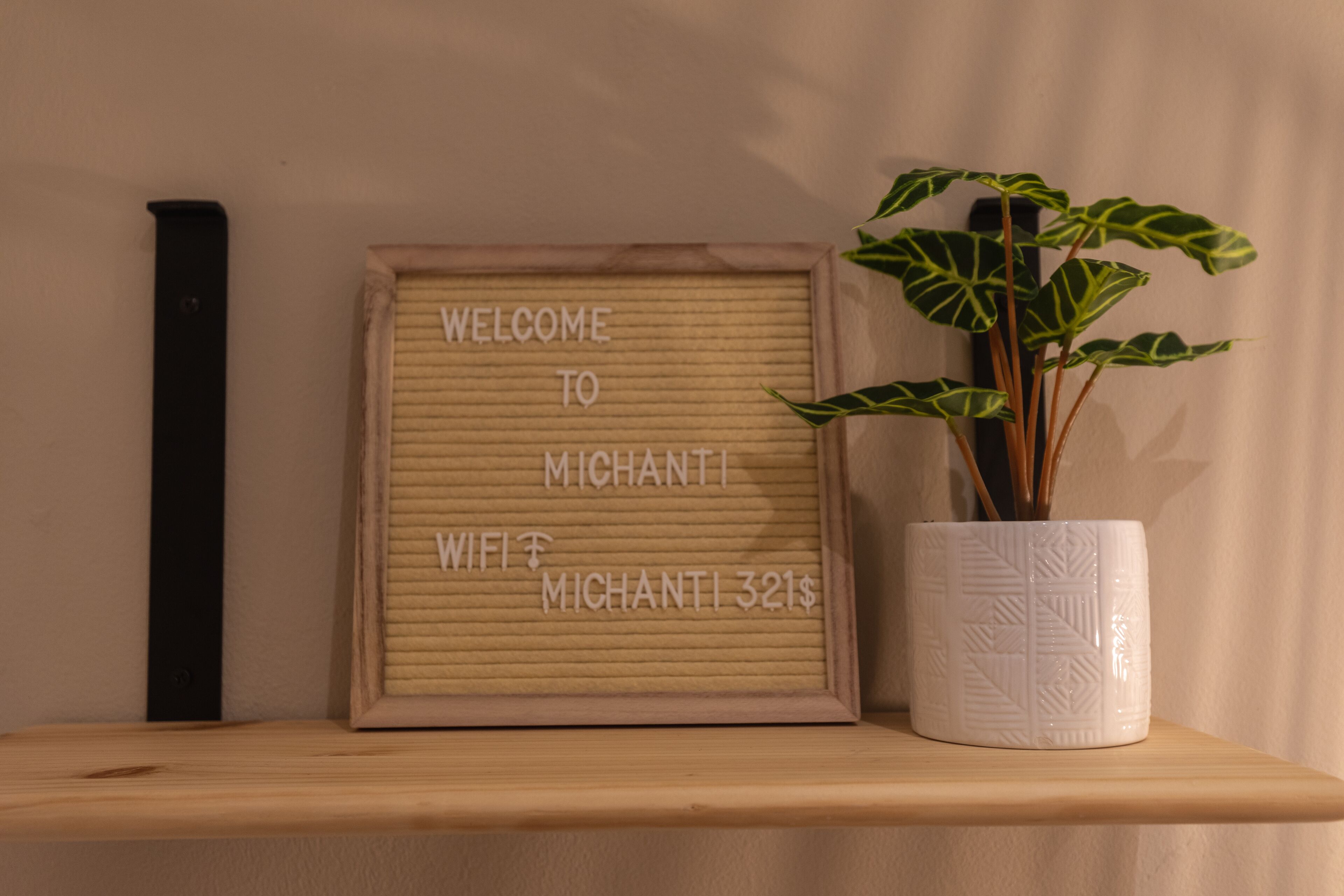 A framed welcome sign with text, a potted plant, and a wooden shelf.