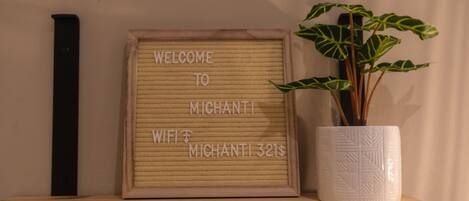 A framed welcome sign with text, a potted plant, and a wooden shelf.