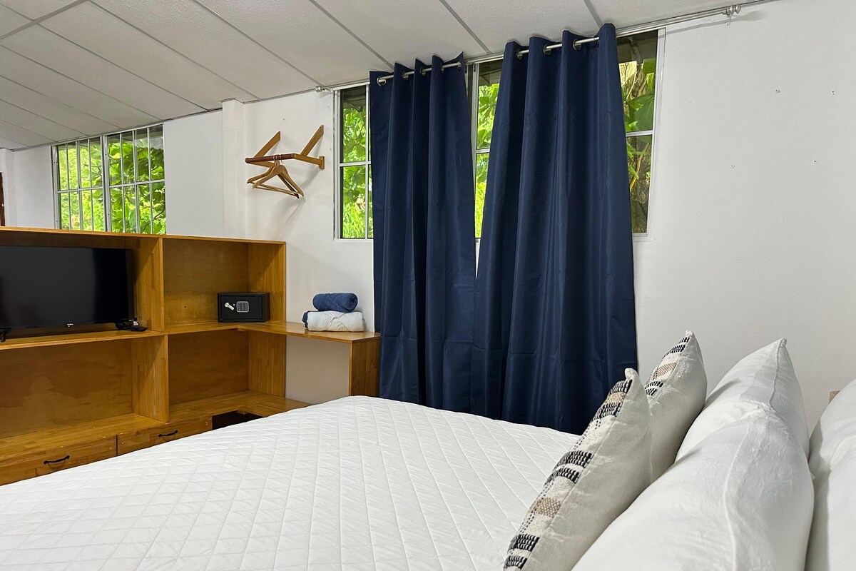 A hotel room with a bed, a TV on a wooden shelf, a safe, and a window with curtains.