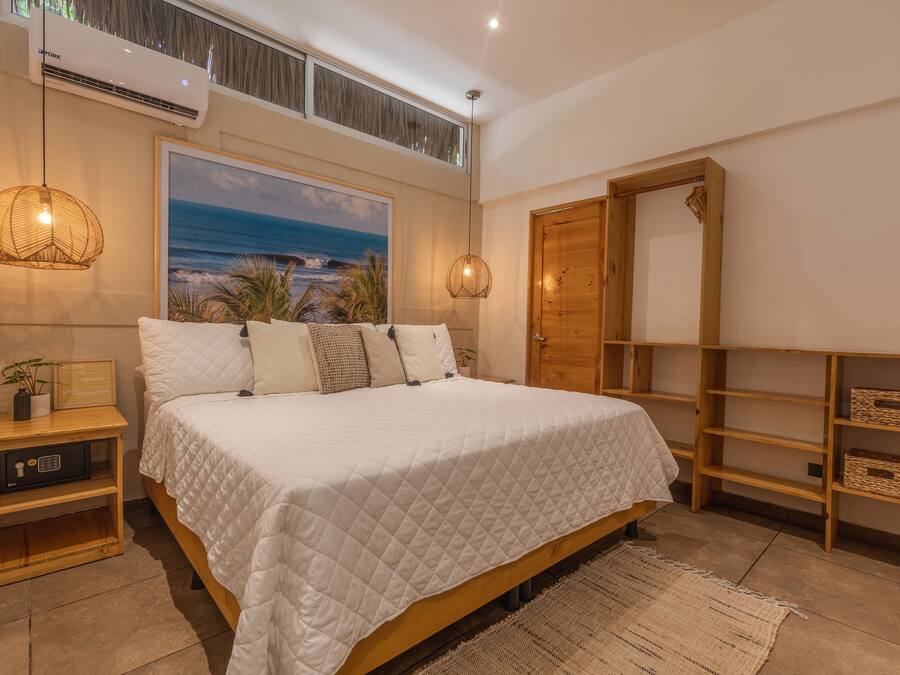 A bedroom with a large bed, a wooden wardrobe, a painting of a beach, and a ceiling fan.