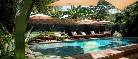 Una piscina al aire libre, sombrillas, sillones reclinables de piscina