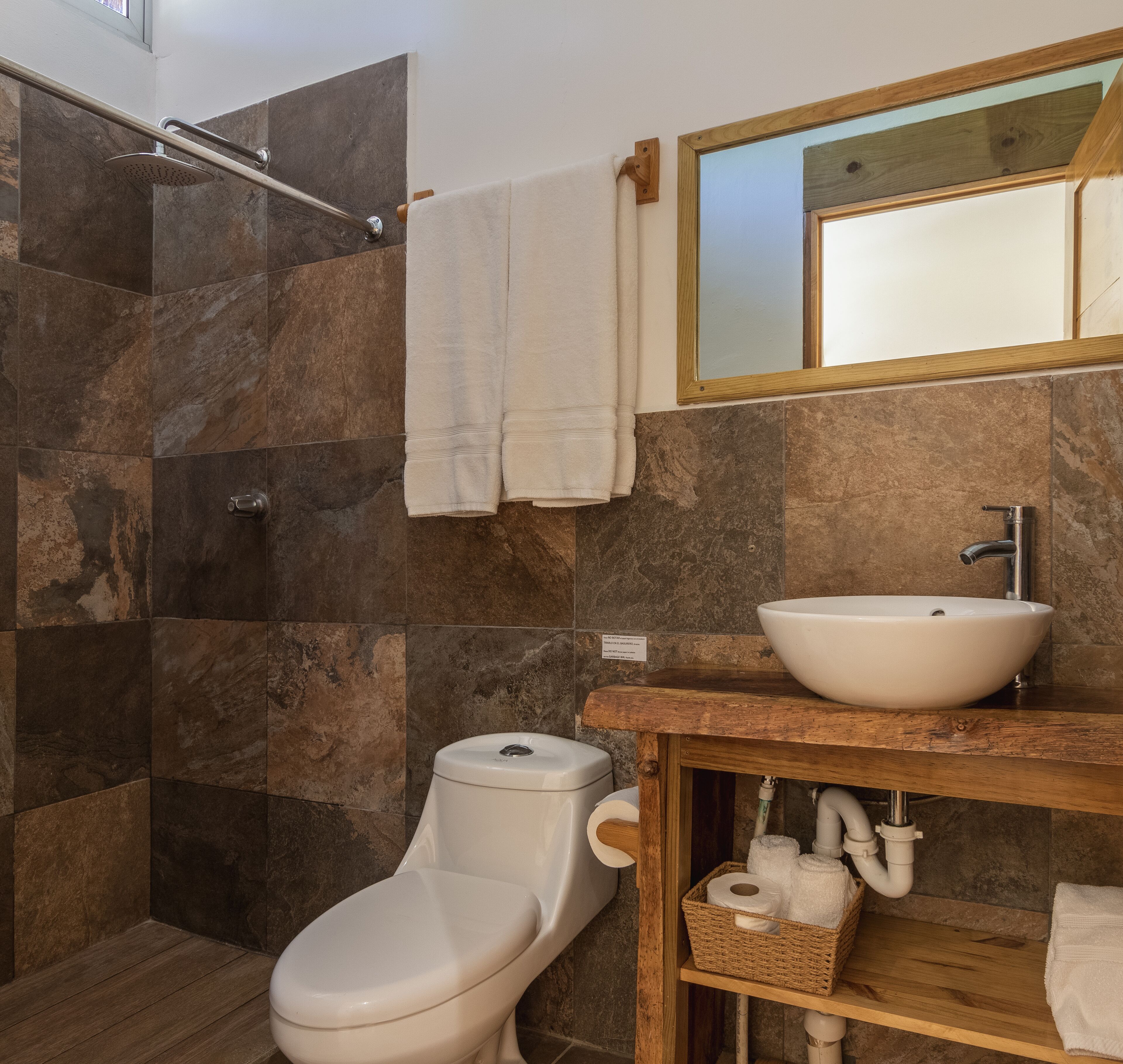 Et badeværelse med bruser, toilet, vask og spejl.
