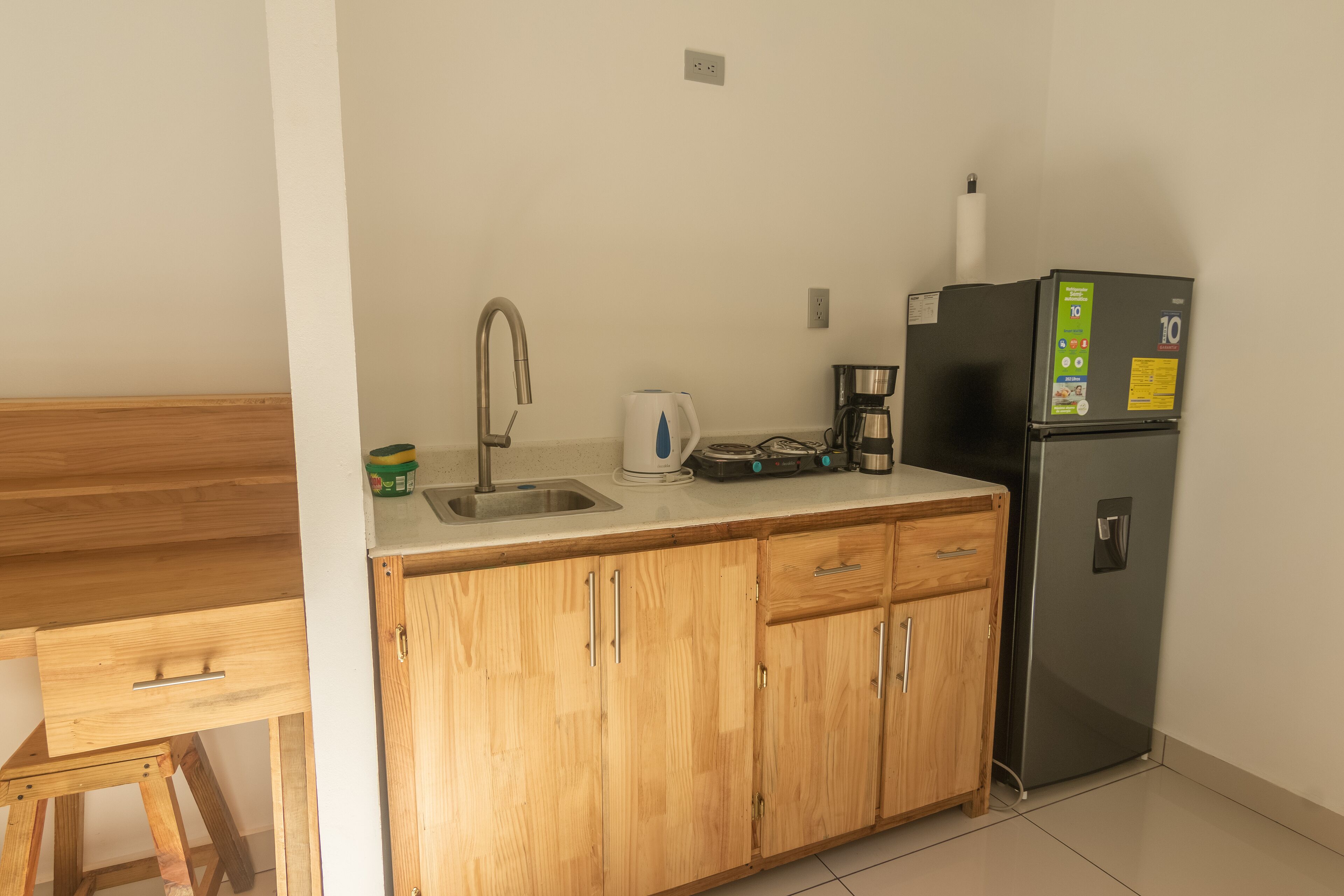 A kitchen with wooden cabinets, a stainless steel sink, a kettle, a coffee maker, and a refrigerator.