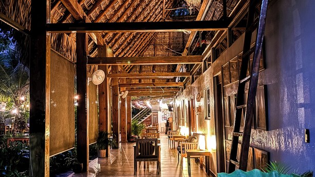 A spacious indoor area with a high ceiling, wooden beams, and a tiled floor. There are several tables and chairs arranged for dining or sitting. - Hotel Michanti (Chiltiupan)