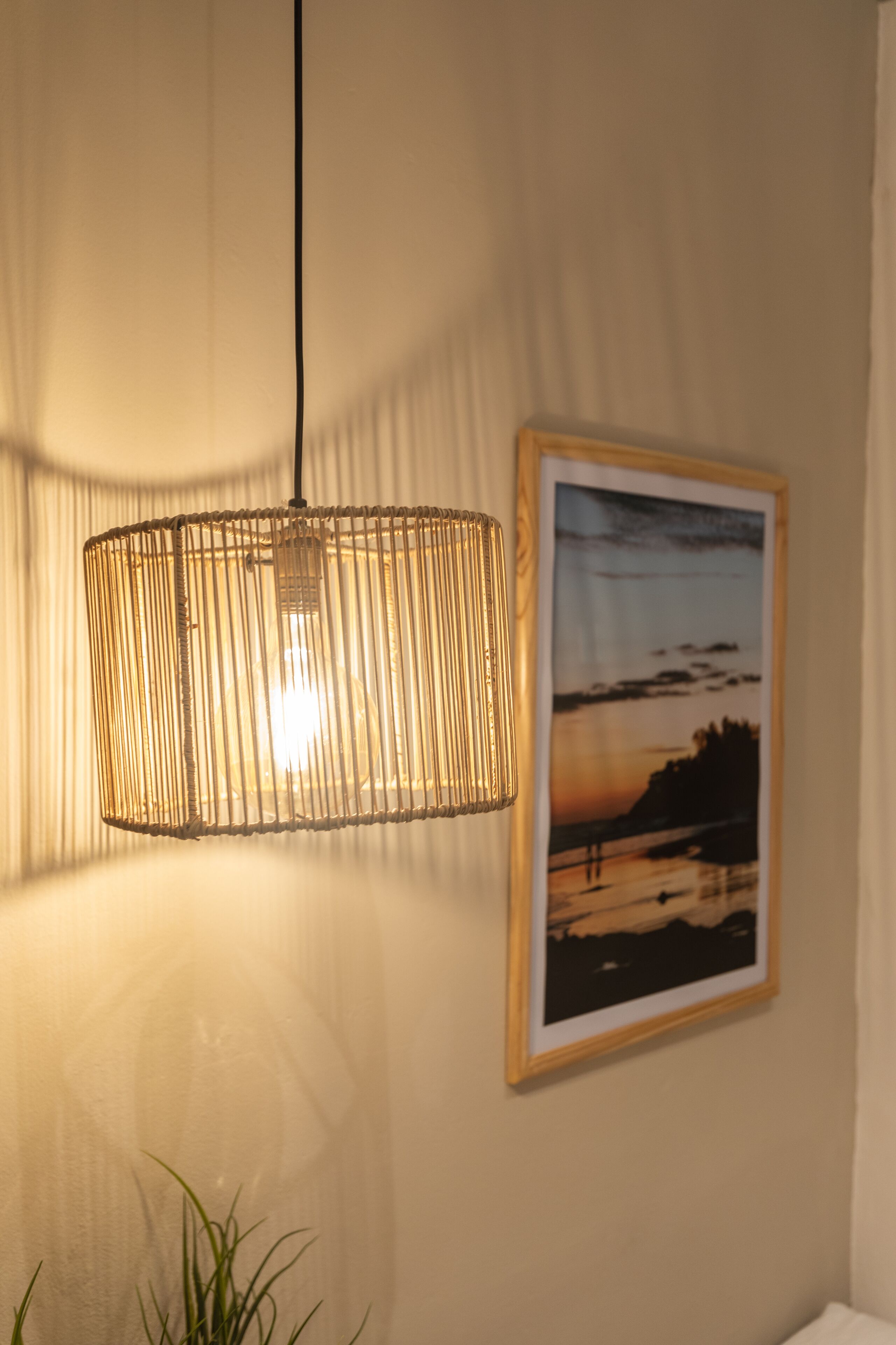 A hanging light fixture with a woven design and a framed picture on the wall.
