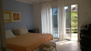 Une chambre à coucher comprenant un lit, une petite table, une chaise et une porte-fenêtre coulissante donnant sur un balcon.