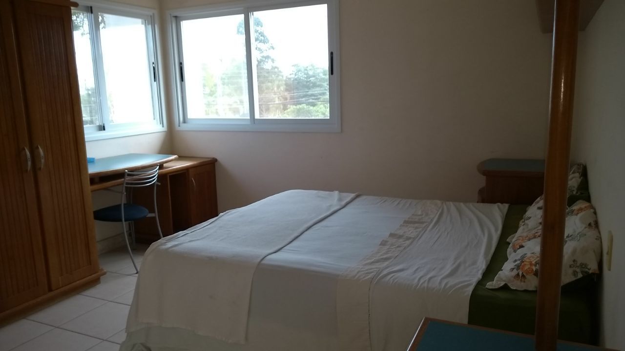 Een slaapkamer met een bed, een bureau en een stoel. Twee ramen zorgen voor natuurlijk licht.
