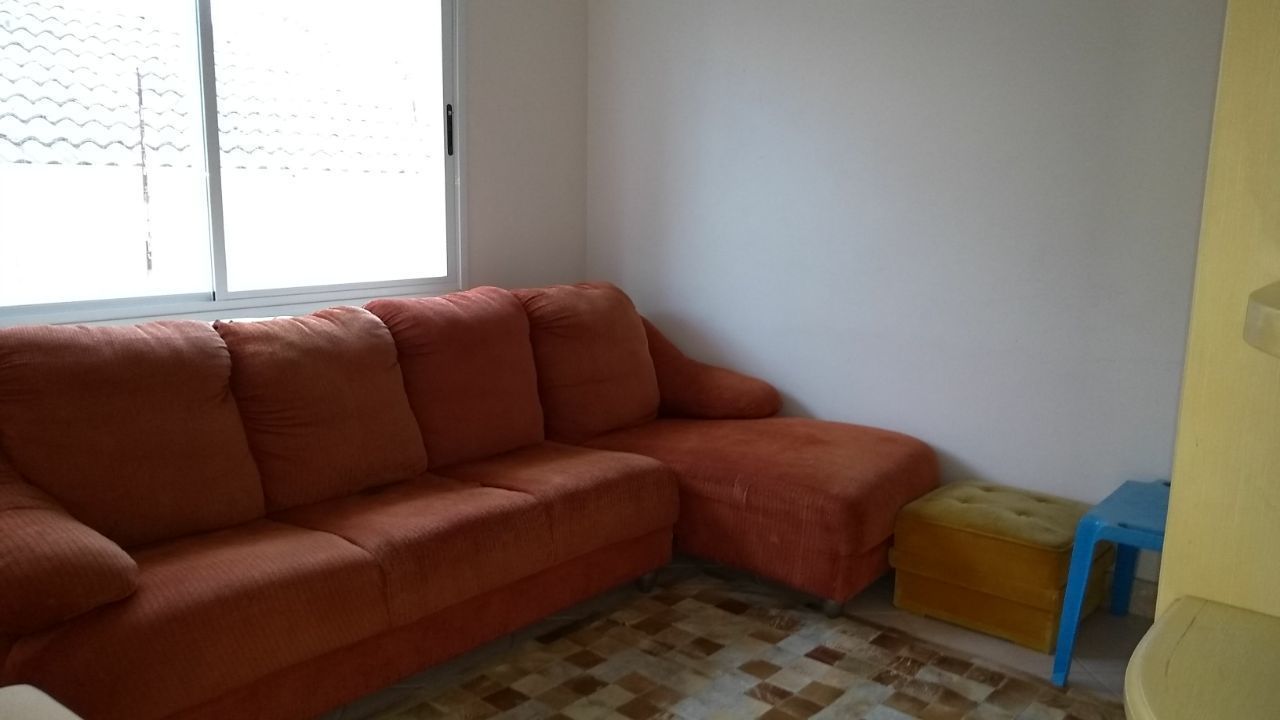 Una habitación de esquina con un sofá rojo, un reposapiés amarillo pequeño y un taburete azul.
