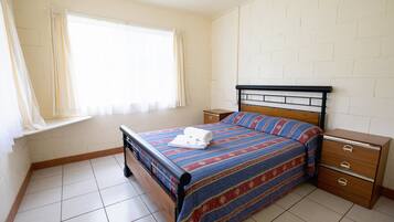 A bedroom with a bed, a nightstand, a dresser, and a window with curtains.