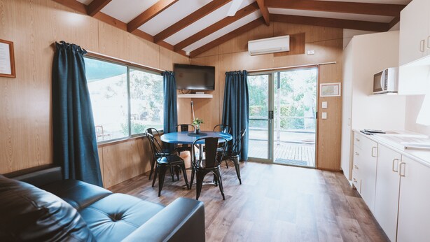 Una cocina moderna con vigas de madera, un comedor con mesa y sillas, y un gran ventanal con cortinas.