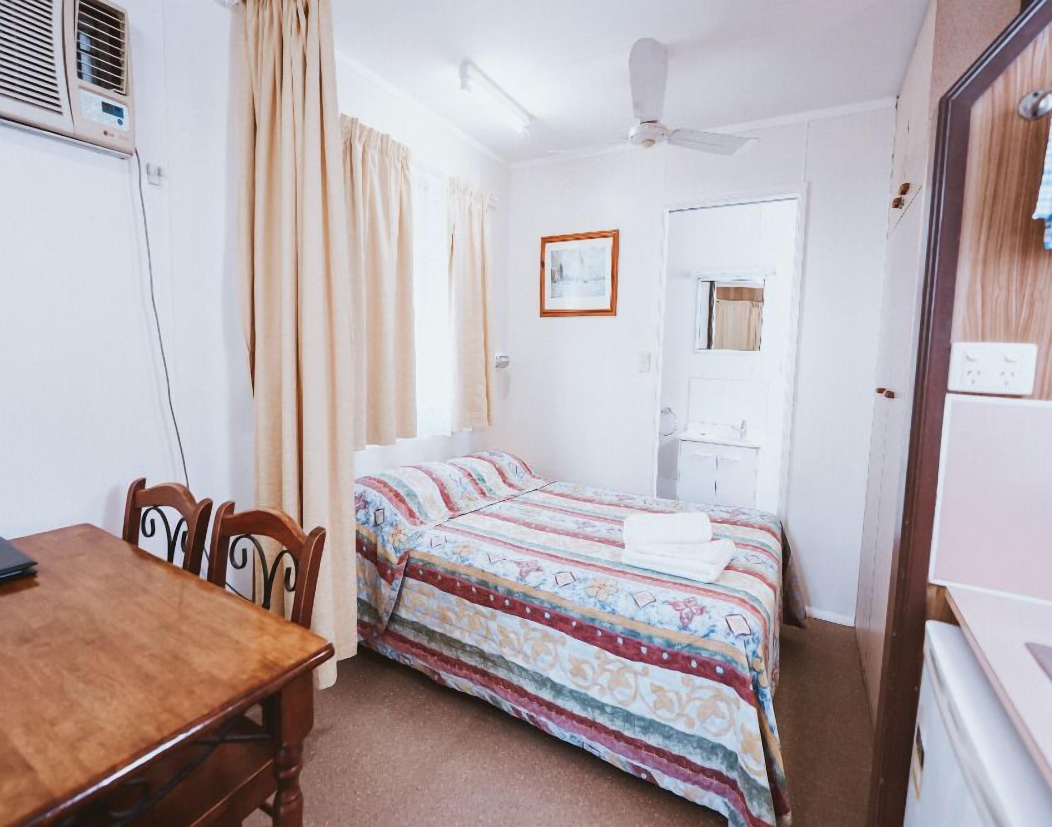 A bedroom with a bed, a desk, a chair, a wardrobe, and a ceiling fan.