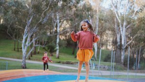 Un niño está de pie sobre una estructura de juegos colorida en un parque con árboles al fondo.
