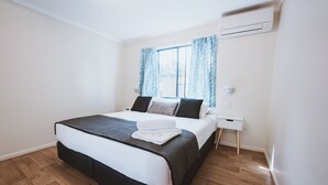 Un dormitorio moderno con una cama grande, paredes blancas, piso de madera y una ventana con cortinas.