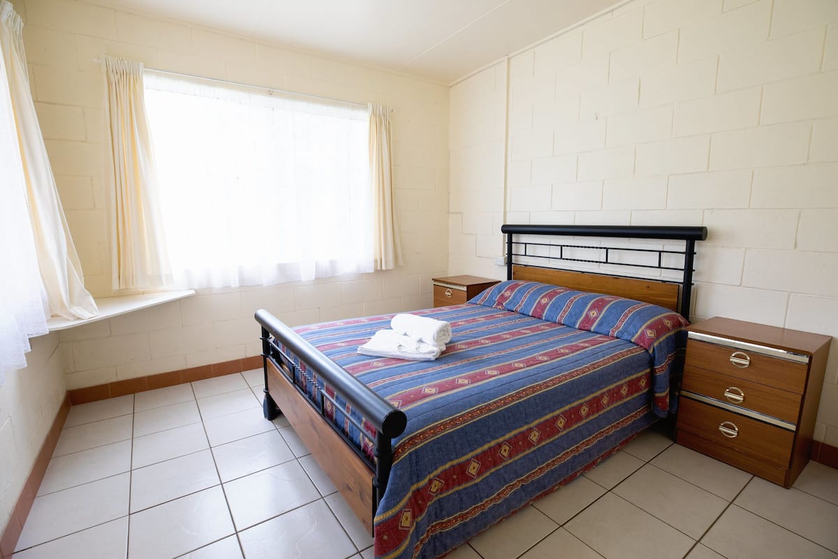 Un dormitorio con cama, mesita de noche, cómoda y ventana con cortinas.