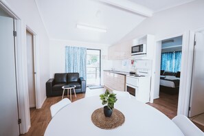 Ein modernes, helles Zimmer mit einem Esstisch, einer schwarzen Ledersofa, einem kleinen Beistelltisch und einer Blumentopf-Pflanze.