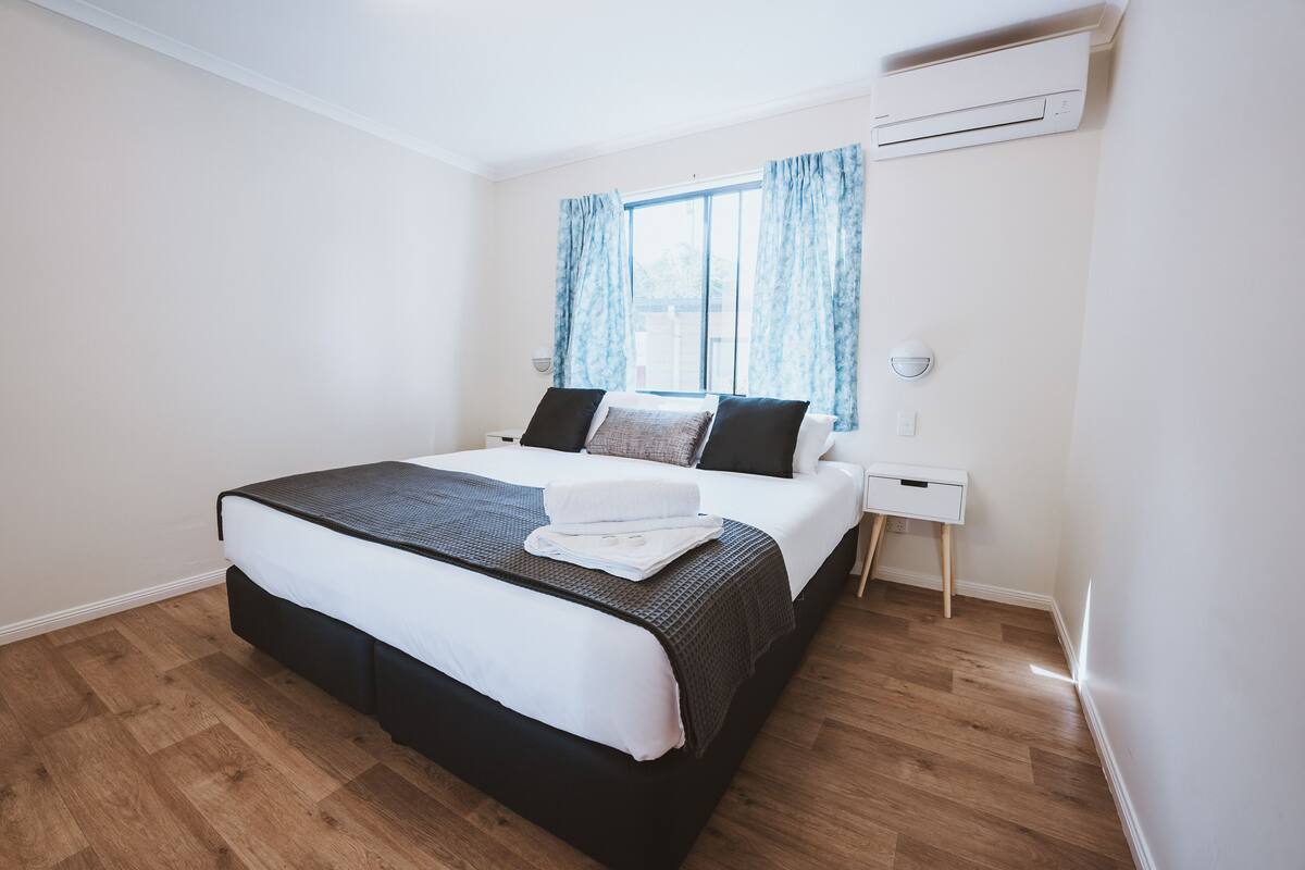 Un dormitorio con cama, mesita de noche y ventana con cortinas.